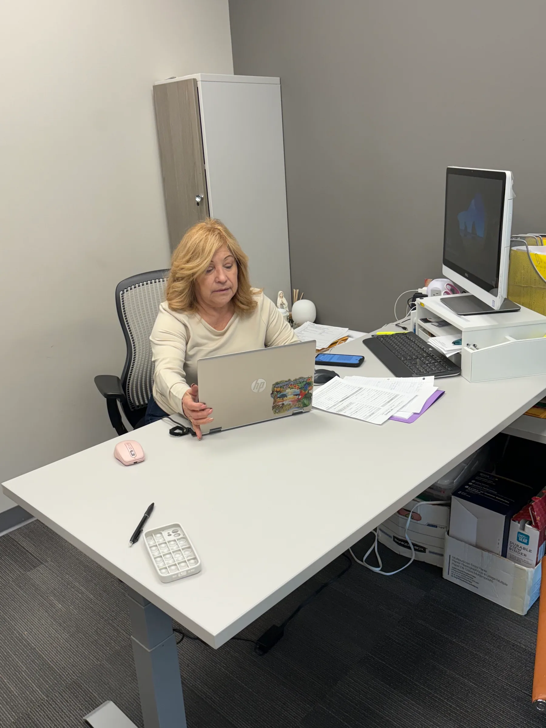 Woman working at office desk with laptop, computer monitor, and tax documents.
